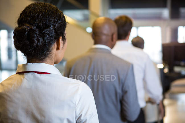 Вид ззаду жіночого персоналу та пасажирів, що стоять у терміналі аеропорту — стокове фото
