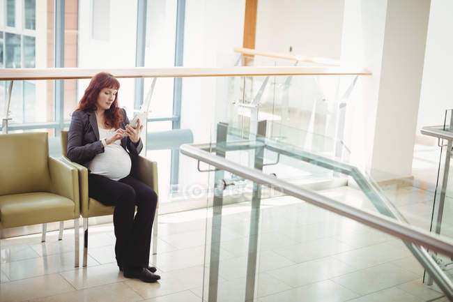 Grávida empresária usando tablet digital perto do corredor no escritório — Fotografia de Stock
