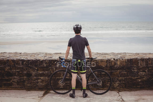Вид сзади спортсмена, стоящего с велосипедом на дороге — стоковое фото