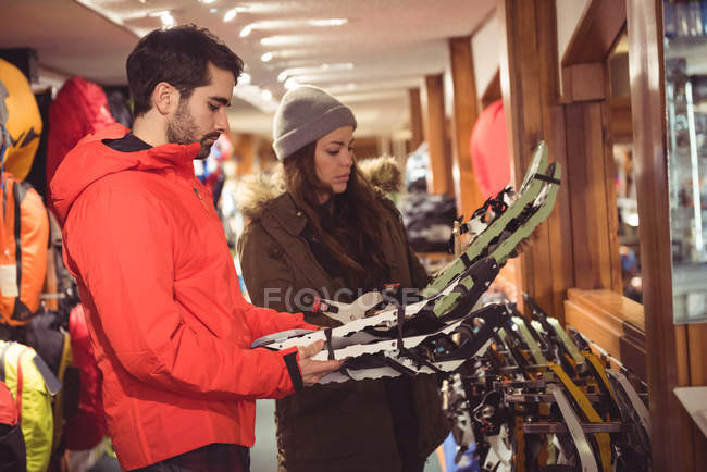 Pareja seleccionando raquetas de nieve juntas en una tienda - foto de stock