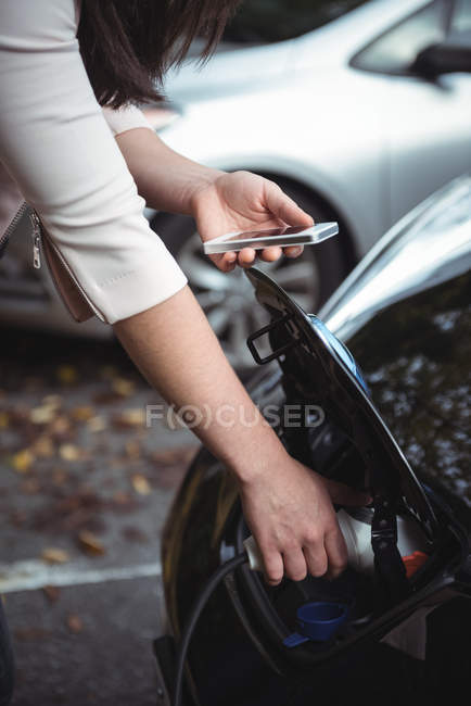 Frau benutzt Handy beim Laden von Elektroauto auf der Straße — Stockfoto