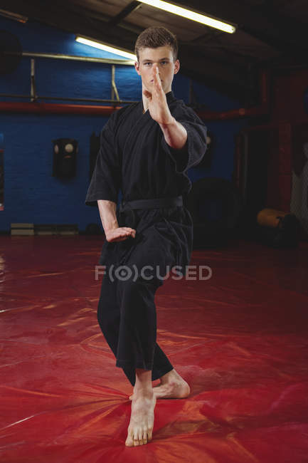 Jeune joueur de karaté adulte effectuant position de karaté dans un studio de fitness — Photo de stock