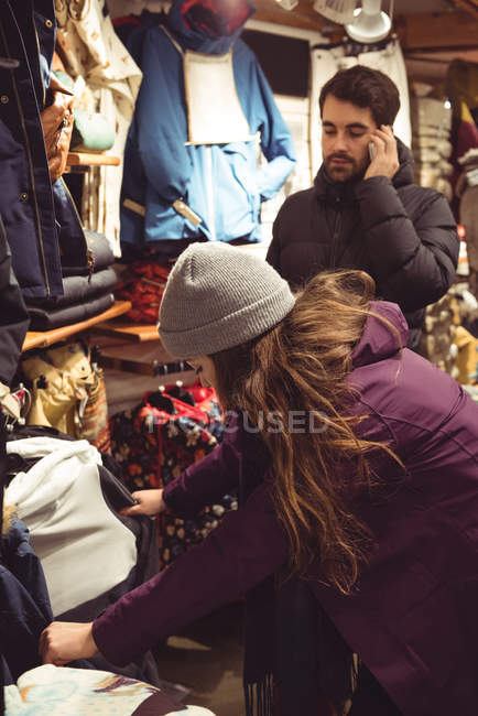 Woman selecting apparel in a clothes shop while man using mobile phone — Stock Photo