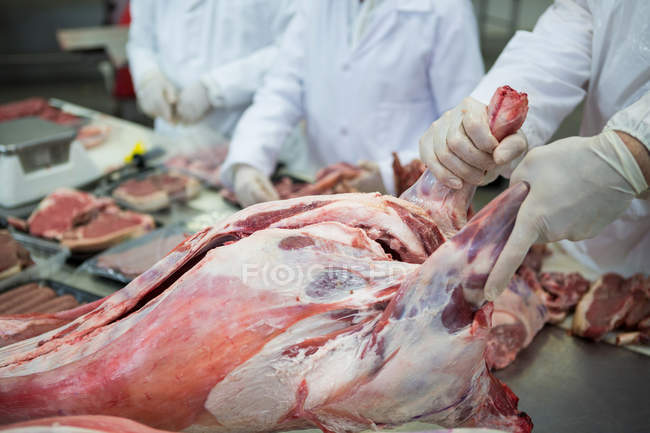 Primer plano de los carniceros que limpian carne cruda en la fábrica de carne - foto de stock