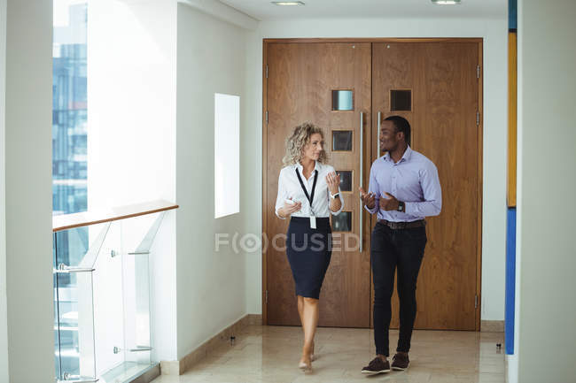 Жіночі та чоловічі бізнес-керівники обговорюють під час ходьби в коридорі в офісі — стокове фото