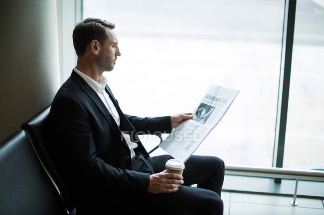 Empresário tomando café enquanto lê jornal na área de espera no aeroporto — Fotografia de Stock