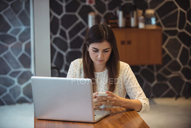 Бізнес-леді, використовуючи мобільний телефон з ноутбуком на столі в кафе — стокове фото