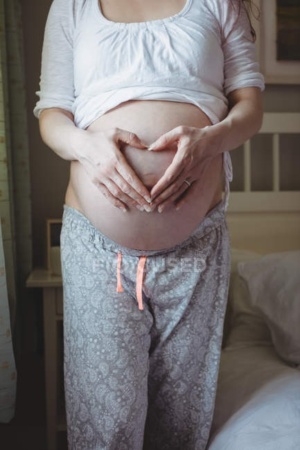 Sección media de la mujer embarazada tocando su vientre en el dormitorio en casa - foto de stock