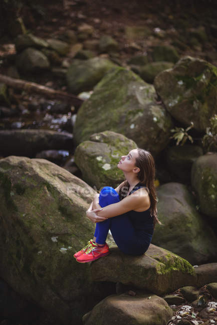 Задумчивая женщина, сидящая на камне в лесу — стоковое фото