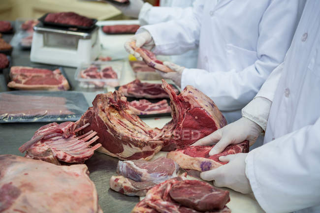 Мясники чистят мясо на мясокомбинате, обрезают — стоковое фото