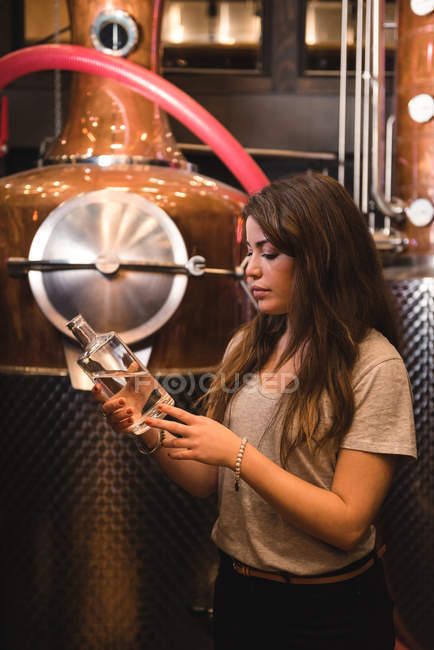 Woman examining a bottle of alcohol in beer factory — Stock Photo