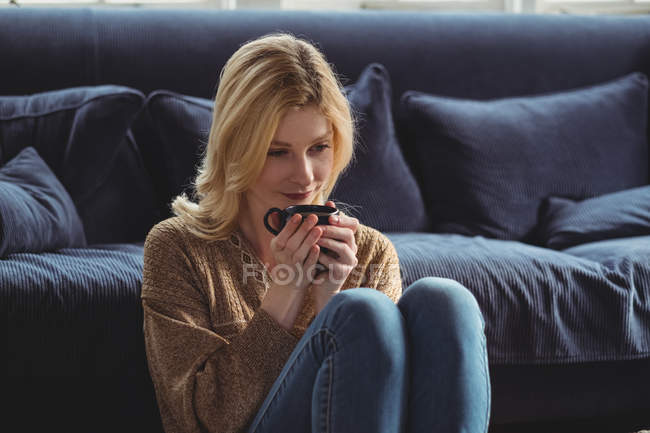 Задумчивая женщина пьет чай в гостиной дома — стоковое фото