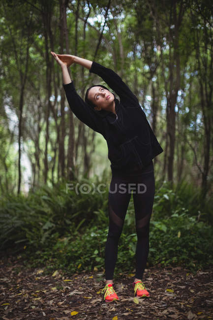 Mujer realizando ejercicio de estiramiento en el bosque - foto de stock