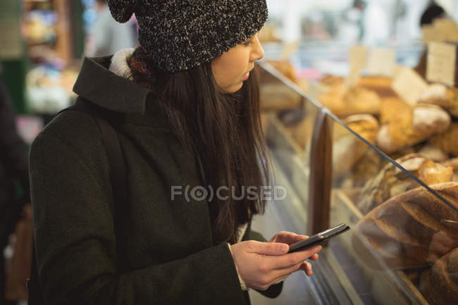Femme utilisant un téléphone mobile près d'un comptoir de boulangerie dans un supermarché — Photo de stock