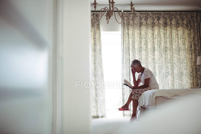 Mujer mayor leyendo libro en el dormitorio en casa - foto de stock