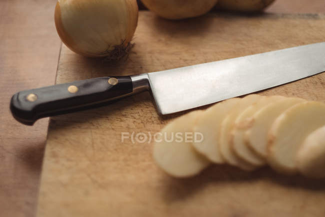Close-up of a onion and sliced potatoes with knife on cutting board — Stock Photo