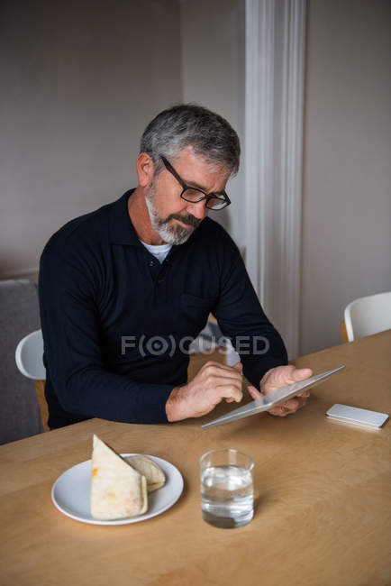 Мужчина сидит за столом и использует цифровой планшет дома — стоковое фото