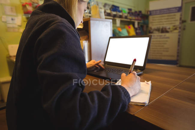 Donna che usa il computer portatile e scrive sul blocco note in ufficio — Foto stock