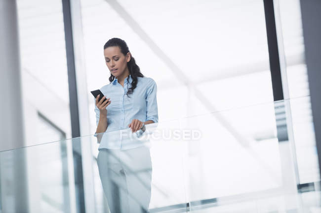 Бізнес-леді, використовуючи мобільний телефон всередині офісної будівлі — стокове фото