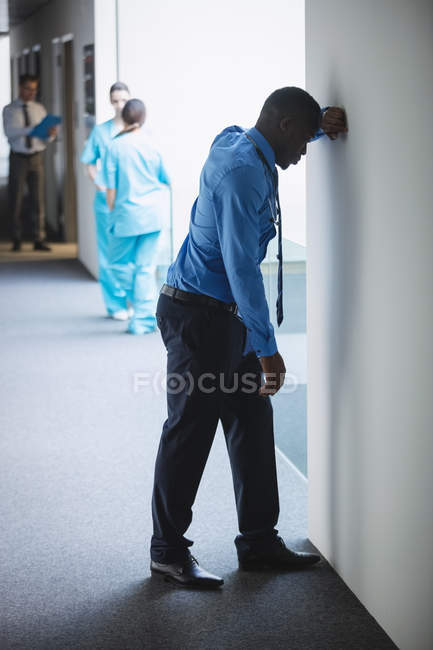 Sad doctor leaning on wall in hospital corridor — Stock Photo