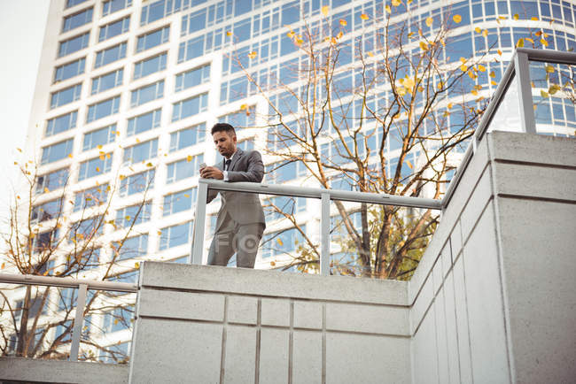 Бизнесмен, использующий мобильный телефон возле офисного здания — стоковое фото