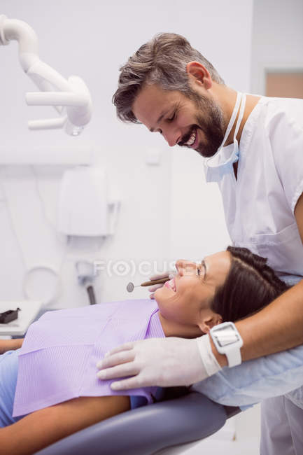 Dentista sorrindo enquanto examina paciente na clínica — Fotografia de Stock