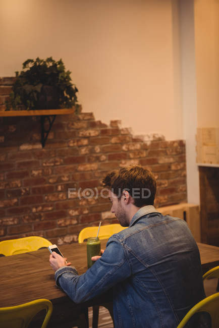 Hombre usando el teléfono móvil mientras tiene jugo en la cafetería - foto de stock