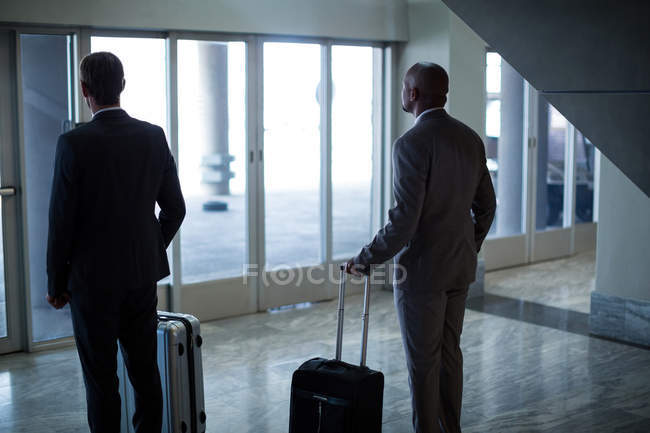 Вид ззаду бізнесменів з багажем, що стоїть в зоні очікування в аеропорту — стокове фото