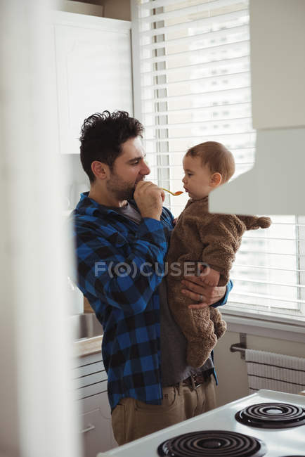 Pai alimentando seu bebê na cozinha em casa — Fotografia de Stock