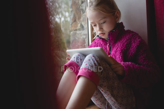 Mädchen sitzt auf Fensterbank und nutzt digitales Tablet zu Hause — Stockfoto