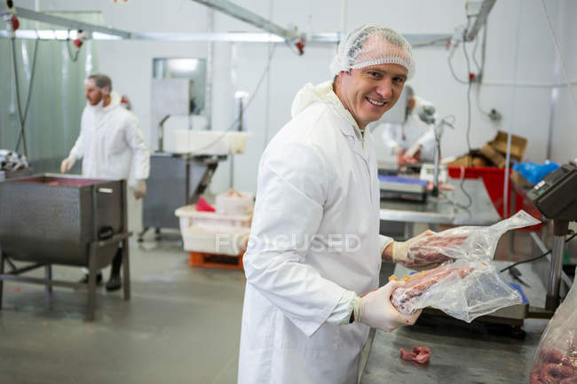 Retrato del carnicero que pesa paquetes de carne en la fábrica de carne - foto de stock