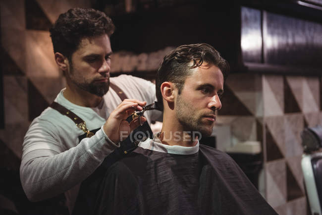 Homme se faire couper les cheveux par un coiffeur avec des ciseaux dans le salon de coiffure — Photo de stock