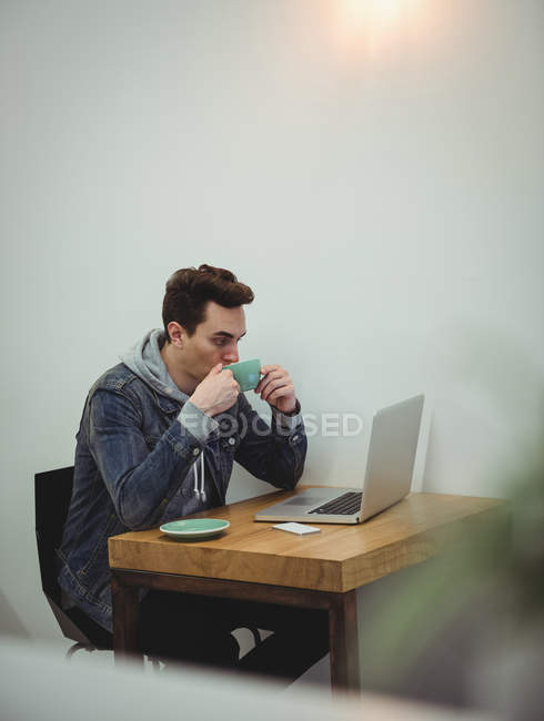 Homme buvant du café tout en regardant ordinateur portable dans un café — Photo de stock