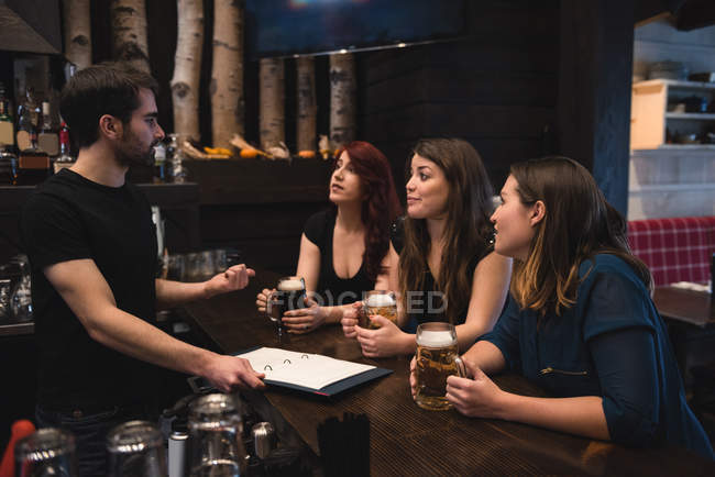 Friends holding beer glasses at bar counter and interacting with bartender — Stock Photo
