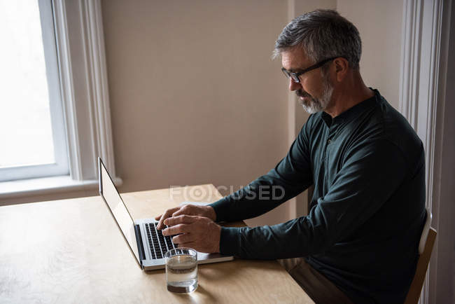 Mann sitzt am Tisch und benutzt Laptop zu Hause — Stockfoto