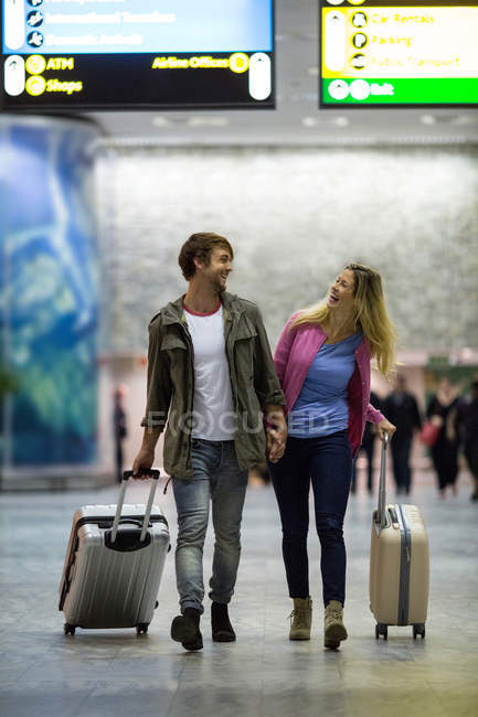 Casal sorridente andando com seus sacos de carrinho no terminal do aeroporto — Fotografia de Stock