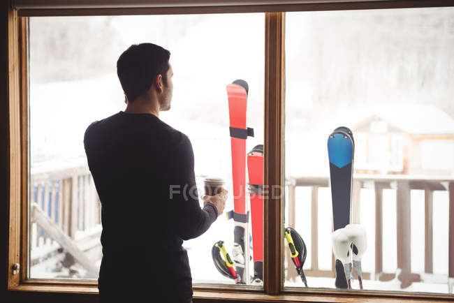 Un hombre frente a una ventana en una cabaña de esquí - foto de stock