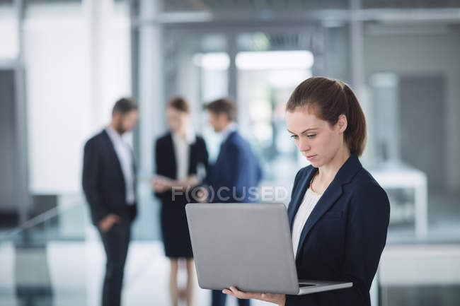 Деловая женщина, стоящая в офисе и использующая ноутбук — стоковое фото