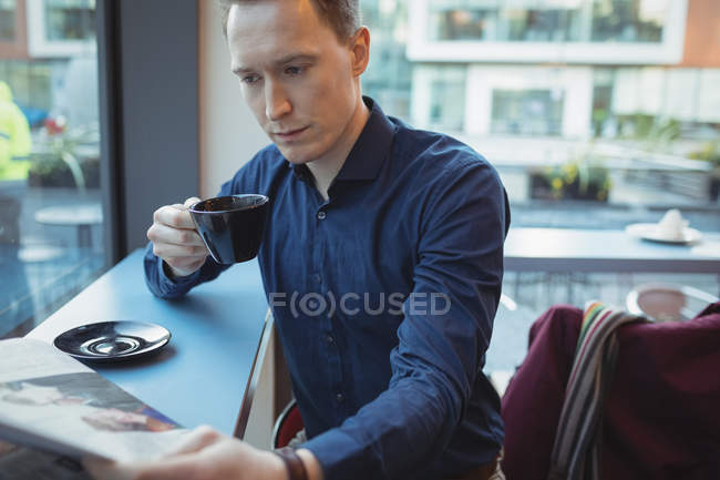 Male executive reading newspaper while having coffee in cafeteria — Stock Photo