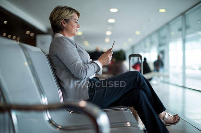Бізнес-леді, використовуючи мобільний телефон в зоні очікування в терміналі аеропорту — стокове фото