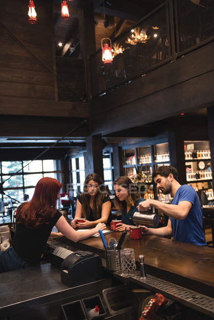 Amigos sosteniendo café en el mostrador del bar e interactuando con el camarero - foto de stock