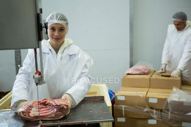 Portrait of female butcher cutting meat with meat cutting machine — Stock Photo