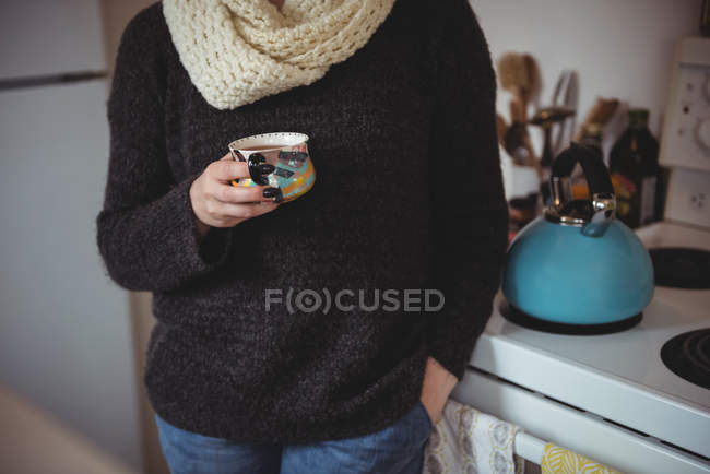 Sección media de la mujer sosteniendo la taza de té en la cocina en casa - foto de stock
