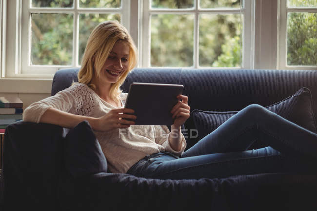 Beautiful woman sitting on sofa with digital table in living room at home — Stock Photo