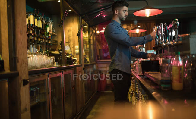 Bartender filling beer from bar pump at bar counter — Stock Photo