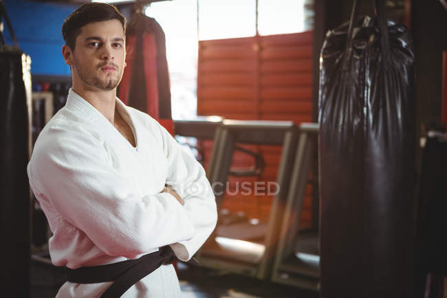 Karate player standing with arms crossed in fitness studio — Stock Photo