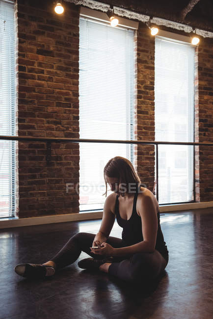 Dancer sitting on floor and using mobile phone in dance studio — Stock Photo