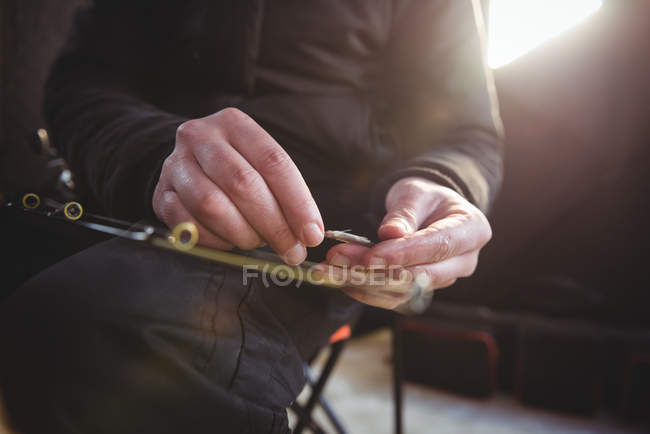 Hands of ice fisherman attaching hook to fishing rod in tent — Stock Photo