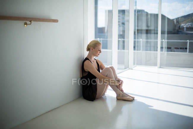 Bailarina deprimida sentada contra la pared en el estudio - foto de stock