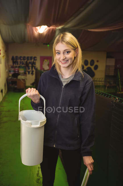 Портрет женщины, несущей корм для собак в пластиковом контейнере в собачьем центре — стоковое фото
